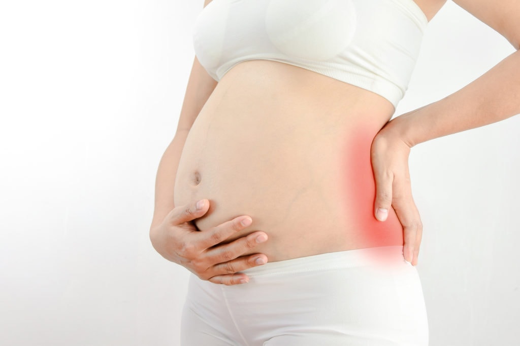 Pregnant woman with a strong pain massaging her backache - pain in red :Pelvic pain or lower back pain in pregnancy